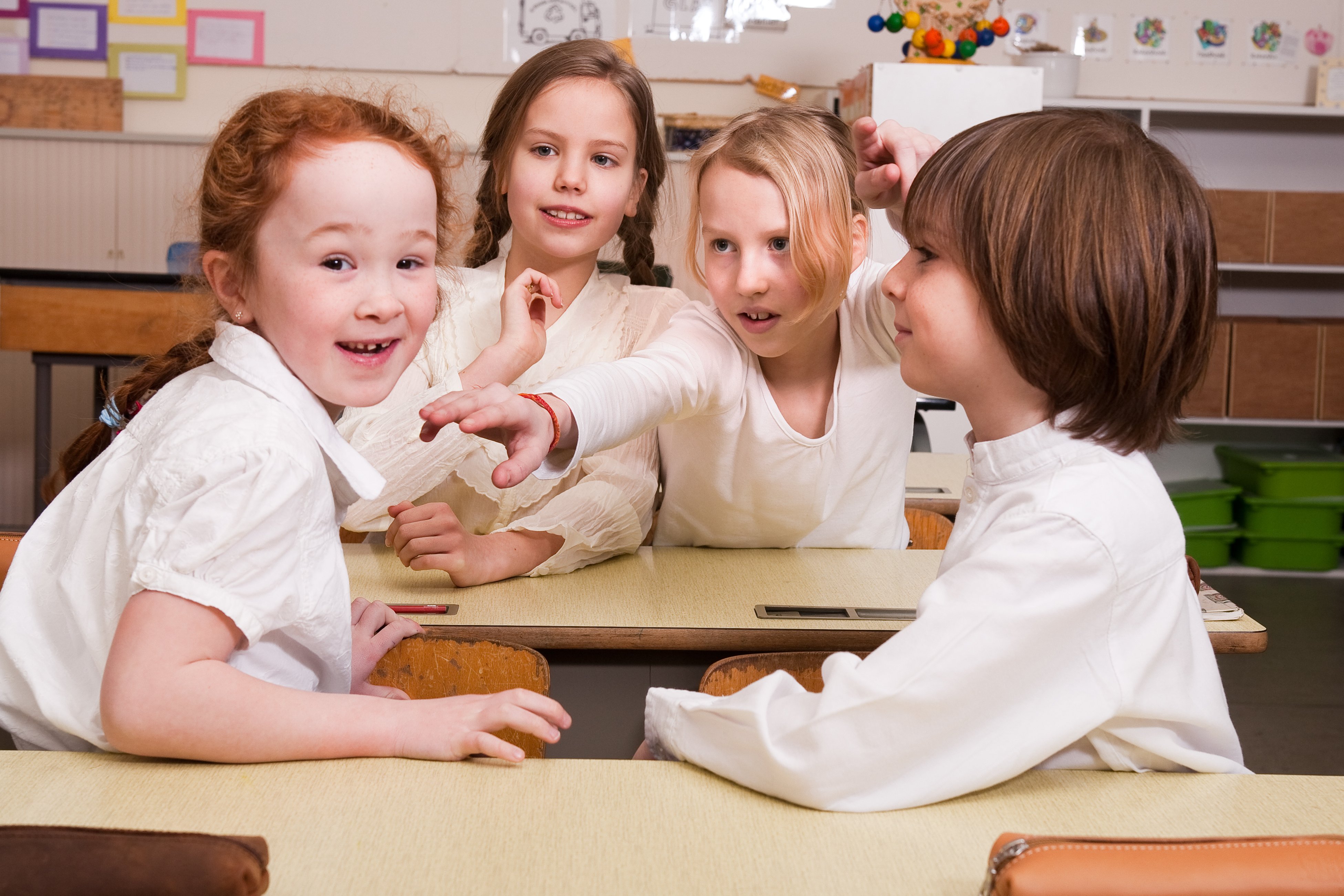 Group of children interacting playfully at their desks in a classroom, highlighting collaboration and social connection.